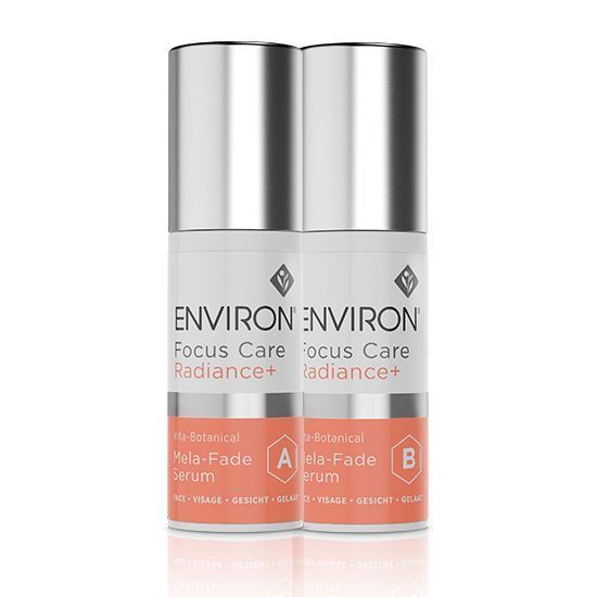 Two cylindrical bottles of Environ Focus Care Radiance+ Vita-Botanical Mela-Fade Serum System A+B are pictured. They have white bodies with metallic silver caps. The labels include text and icons, with sections marked "A" and "B" denoting two different serum formulations aimed at improving skin tone and addressing pigmentation issues.