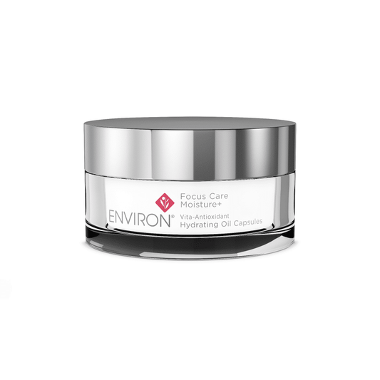 A small, round, silver-lidded container of Environ Focus Care Moisture+ Vita-Antioxidant Hydrating Oil Capsules. The label is white with the product name and branding in grey and pink font. Packed with antioxidants and vitamins, the reflective container stands out against a plain white background.