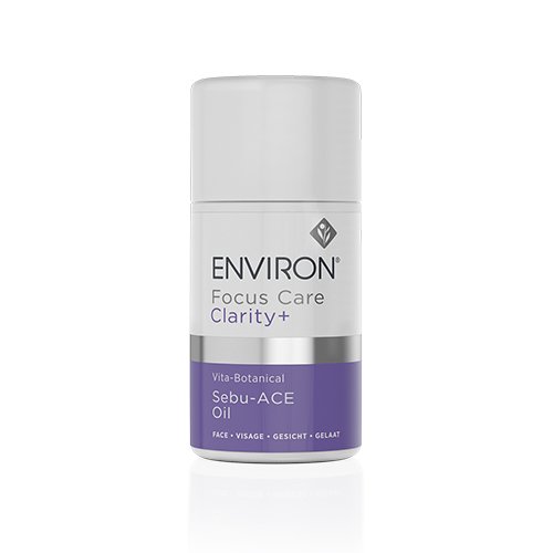 A white cylindrical bottle labeled "Environ Clarity+ Vita-Botanical Sebu-ACE Oil" with a purple band near the base. Designed for breakout-prone skin, the label includes text for face, visage, gesicht, and gelaat. The bottle is standing upright on a reflective white surface.